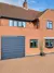 An orange brick house with a balcony, anthracite grey window frames and an anthracite grey roller garage door.