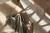 Close up from above of wooden dining chair with wicker seat pulled out from under a pale wood table, on a pale marble tiled floor with rays of light on the chair and floor, casting shadows.