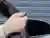 Hand coming out a car window holding a remote control fob which is pointing at the closed garage door ahead.) 