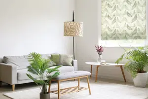 Lounge in neutral colours with cream rug, mink sofa to left, cream lamps, two large planters with ferns and window dressed in Roman blind in pale green with green fern pattern.